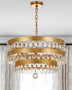 a chandelier hanging from the ceiling in a living room with curtains and drapes