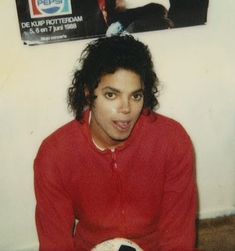 a man sitting on the floor with a soccer ball in his hand and a poster behind him