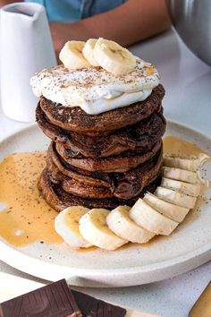 a stack of pancakes with bananas and whipped cream on top, sitting on a plate