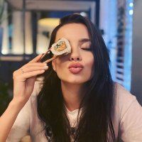 a woman is eating sushi with chopsticks in front of her eyes and looking at the camera