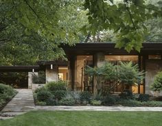 a modern house surrounded by lush green trees and shrubbery in the foreground is a stone path leading to it