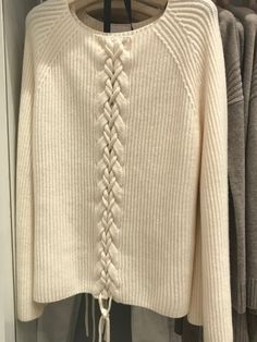 a white sweater with braids hanging on a hanger in front of some clothes