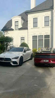 two cars are parked in front of a large white house on a driveway next to a red car