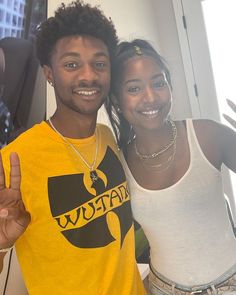 a man and woman standing next to each other in front of a window smiling at the camera