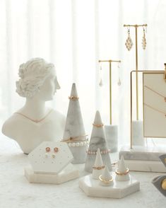 a white table topped with jewelry and a busturine in front of a window