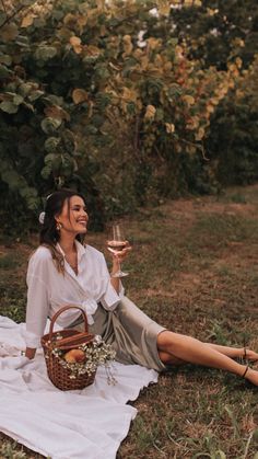 a woman sitting on the ground holding a glass of wine in her hand and smiling