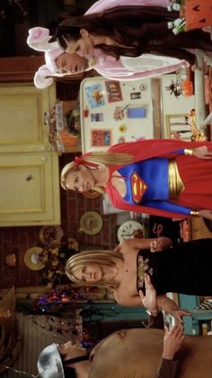 two women standing next to each other in front of a kitchen with superman dolls on the counter