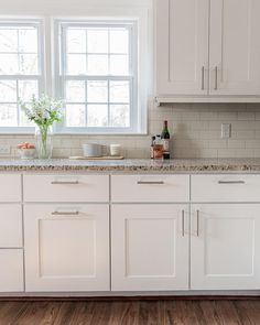 a kitchen with white cabinets and marble counter tops is pictured in this image, there are two vases on the window sill