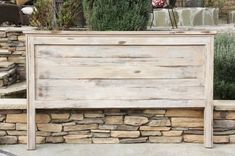 a wooden bench sitting in front of a stone wall next to a planter filled with flowers