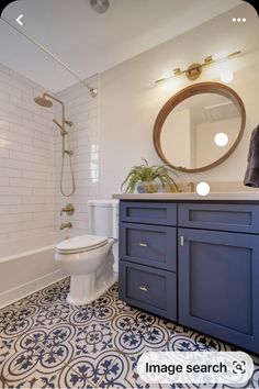 a white toilet sitting next to a bath tub in a bathroom under a round mirror