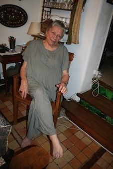 an older woman sitting in a chair with her foot up on the floor and looking at the camera