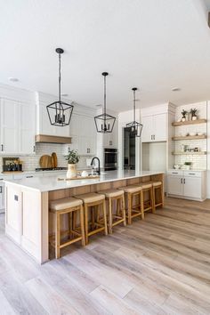 a large kitchen with white cabinets and wooden flooring is pictured in this image, there are four stools at the center of the island