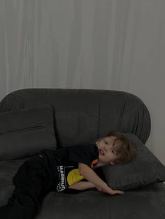 a young boy laying on top of a gray couch next to a yellow banana peel