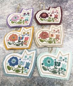 four embroidered heart shaped ornaments hanging from hooks on a stone surface with flowers and leaves