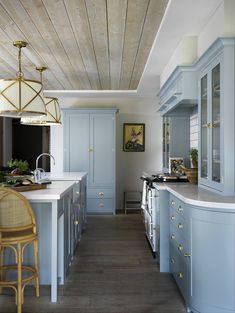 a kitchen with blue cabinets and white counter tops next to a dining room table in front of a wooden ceiling