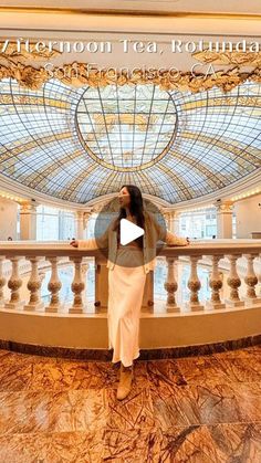 a woman standing on top of a balcony in front of a glass ceilinged building