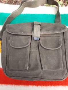 "This simple military style waxed canvas shoulder bag is made from heavy 100% cotton canvas and is treated with a beeswax blend that repels water; treating canvas with wax is a method used since the 1920's to make the material water resistant. It features one large main compartment and two front pockets with hook and loop closures. The main flap closes with a strap and a metal fold over style buckle. The bag measures approximately 10\" across by 8\" tall and 3.5\" wide with a strong 1.5\" wide a Vintage Canvas Satchel With Pockets, Military Style Canvas Bag With Pockets, Vintage Canvas Shoulder Bag With Pockets, Khaki Waxed Canvas Bag With Adjustable Strap, Military Canvas Shoulder Bag For Outdoor, Military Canvas Shoulder Bag For Everyday Use, Hobo Canvas Bag With Pockets, Military Style Canvas Shoulder Bag, Outdoor Khaki Cotton Shoulder Bag