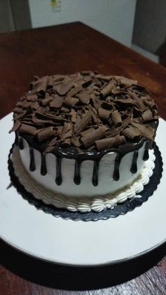 a chocolate cake with white frosting and drizzled on top sitting on a wooden table