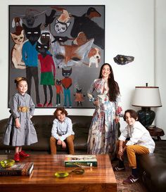 a woman standing next to two children in front of a painting on the wall behind her