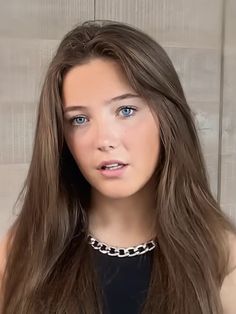 a woman with long brown hair wearing a black top and silver chain around her neck