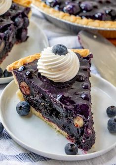 a slice of blueberry pie on a plate with whipped cream and fresh blueberries