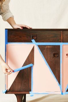 a woman is painting a cabinet with pink and blue tape on it's sides