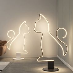 three illuminated cats sitting on pedestals in a room with white walls and flooring