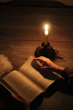 a person reading a book with a candle in the background