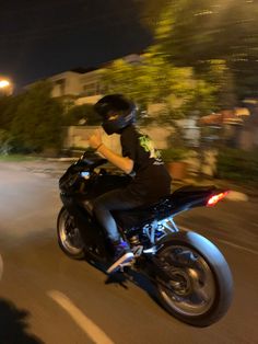 a man riding on the back of a black motorcycle down a street at night time