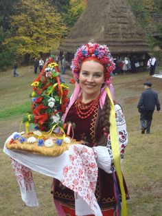 a woman dressed in folk garb holding a tray with food and flowers on it