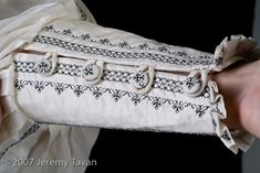 a person holding a piece of cloth in their right hand and wearing a white dress with black embroidery on it