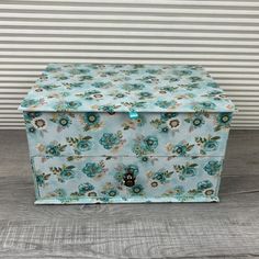 a blue flowered box sitting on top of a wooden table next to a striped wall