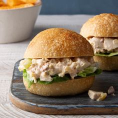 two chicken salad sandwiches with lettuce and cheese on a cutting board next to fries