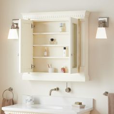 a white bathroom sink sitting under a mirror next to a wall mounted medicine cabinet with lights on it