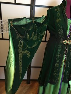 a green and black costume is hanging on a rack in front of a white wall