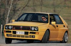 a yellow car driving down a road next to a forest