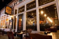 the outside of a restaurant at night with tables and chairs in front of the window