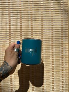 a person holding a blue coffee mug in front of a wicker wall with their shadow on it