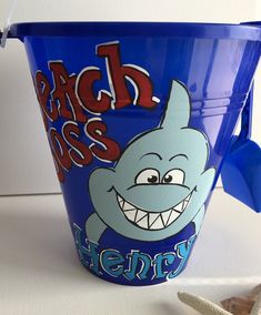 a blue bucket with a shark design on the side and starfish in the background