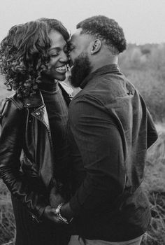 a man and woman standing next to each other in front of tall grass with trees