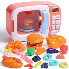 a toy microwave oven with various toys surrounding it on a white surface and in the background, there is an assortment of food