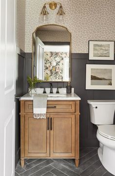 a white toilet sitting next to a wooden cabinet in a bathroom under a large mirror