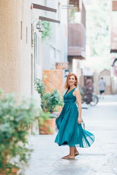 a woman in a teal dress is walking down the street with her hand on her hip