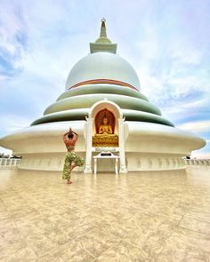 a person standing in front of a large building with a buddha statue on it's side