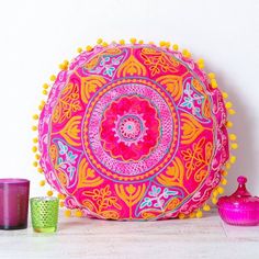 a pink and yellow decorative pillow sitting on top of a table next to two cups