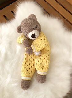 a crocheted teddy bear laying on top of a white fur rug with its eyes closed