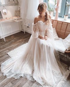 a woman is sitting on a couch in a white wedding dress with off the shoulder sleeves