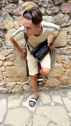 a man sitting on a stone wall with his back to the camera, wearing sandals and a fanny bag