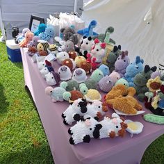 there are many stuffed animals on the table at this outdoor event, including teddy bears