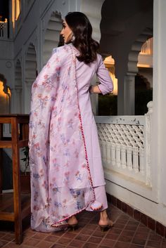 a woman in a long pink dress standing on a porch next to a white building